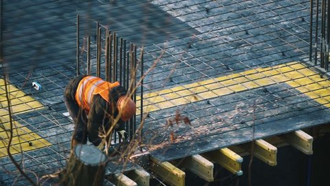 Slow motion builder cuts rebar with an angle grinder at construction site