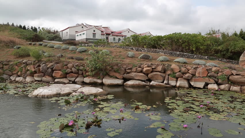 A historical village near a pond in Penghu, Taiwan. The pond has lotus flowers, leaves and stones around it.