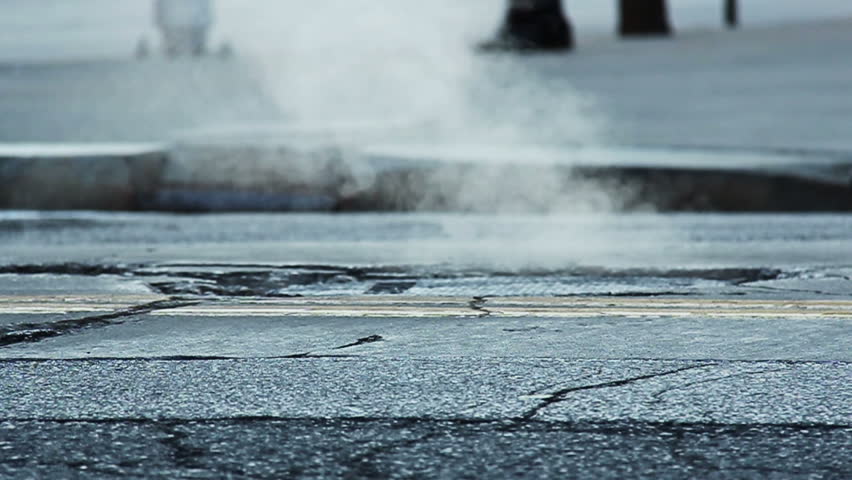 Slow motion shot of steam coming from a manhole in a street.