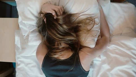 Tip view of depressed young woman lying face down on the bed. Crying girl shaking head and pulling at hair with anger.