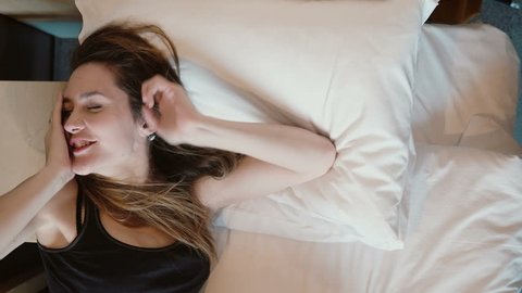Fresh happy woman lying in bed and stretching. Attractive girl wakes up in the morning, smiling.