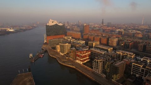 Aerial drone shot of Hamburg harbor in beautiful morning light. View of the Elbphilharmonie, Hafencity, Grasbrookhafen and "Michel" - St. Michaelis Church. A ferry boat is leaving a pier.