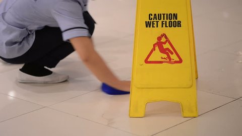 Sign showing warning of caution wet floor and Worker with cloth cleaning hall floor of public business building.