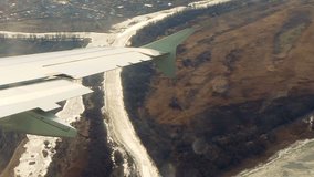 Aviation adventure: dramatic aerial perspective captures aircraft wing extending over majestic terrain, showcasing sleek engineering and soaring motion. Winding river meanders through landscape with frosty banks and vibrant ice patches, creating striking contrast against earthy tones and muted palette. Below unfolds tapestry of land with soft greens and browns, indicating seasonal transition between fall and springtime. Jagged silhouettes of barren trees dot surrounding topography while faint urban structures suggest proximity to civilization in distance. Natural soft lighting casts gentle glow across scene, imparting tranquil yet dynamic feeling of exploration and airborne discovery. Perfect for travel campaigns, aviation marketing, or adventure blogs embracing both industrial marvels and natural splendor from unique vantage point. - Powered by Shutterstock - Get 15% off with code: PIKWIZARD15