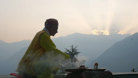 A Hindu old man in yellow national costume offering special spiritual prayer to god in the foothills of the Himalayas, Kullu Valley, India