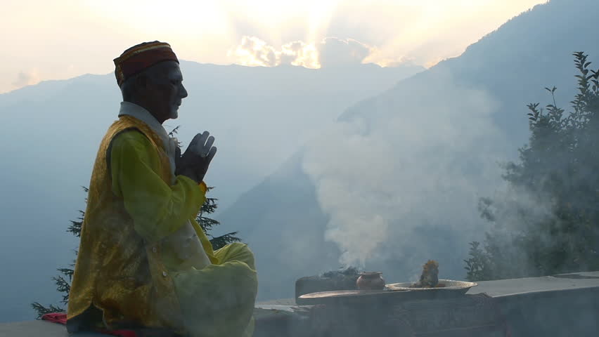 A Hindu old man in yellow national costume offering special spiritual prayer to god in the foothills of the Himalayas, Kullu Valley, India