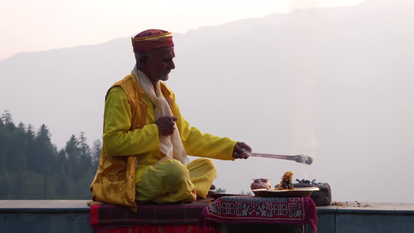 A Hindu old man in yellow national costume offering special spiritual prayer to god in the foothills of the Himalayas, Kullu Valley, India