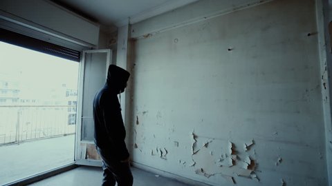Hooded depressed young man in empty abandoned house.A young man wearing a hoodie inside a derelict destroyed apartment in the city