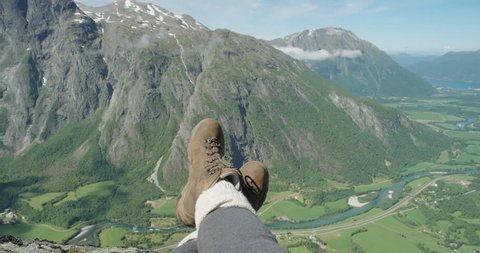 Close up hiking boots of Independent Woman traveller on top of mountain looking at view Hiker girl dangling feet over edge of cliff enjoying vacation travel adventure nature Romsdal Valley Norway