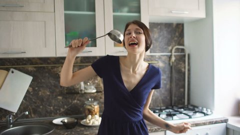 Funny woman housewife cook dance and sing with big ladle while cooking in modern kitchen at home