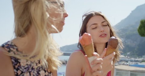 Young women eating ice cream on beach Best friends licking Italian Gelato outdoors in summer sunshine Girls enjoying European vacation travel adventure Amalfi Coast  Italy