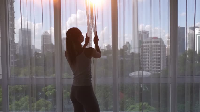 Super slow motion. Young woman uncover the big window and looking out her apartment on the city buildings. Sunrise in the city. Royalty-Free Stock Footage #24373268