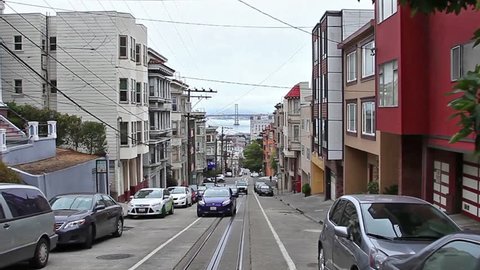 San Francisco, California, United States - August 17, 2016: Cable Car, Powell-Manson lines, of San Francisco, in Jackson street along old historical houses, Oakland Bay Bridge on the horizon.