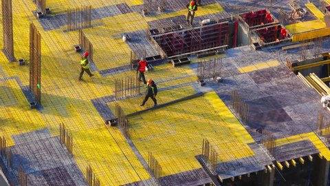 Top view of a group of construction workers at construction site. Builders laids metal reinforcements for the new floor slabs. Zoom out effect from the bottom point. Time lapse