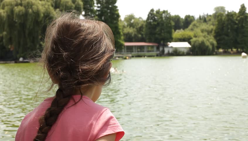 Little girls throwing bread bits to swimming geese. Sunny hot summer day.