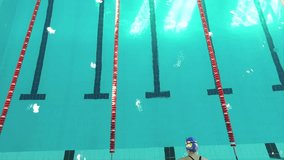 Aerial top view of female swimmer jumps off starting block into pool water HD video. Professional athlete training swimming