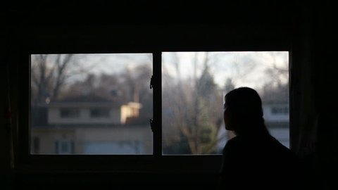 Silhouette of woman looking out window at neighborhood, video