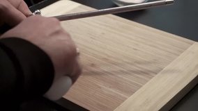 Hands sharpening knife over cutting board with honing steel
