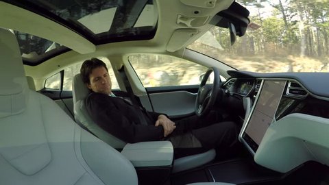 AUTONOMOUS TESLA CAR, FEBRUARY 2016:  Businessman sleeping behind the self-driving steering wheel of an autonomous electric Tesla car. Man fell deeply asleep while driving along the countryside road