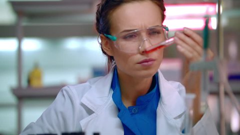 Woman chemist doing chemical test in chemistry laboratory. Closeup of female chemist working with chemical liquid in test tube. Chemistry scientist mixing chemical liquid in flask in chemical lab