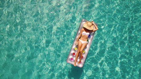 Aerial - Young woman enjoying summer on inflatable mattress in crystal clear water