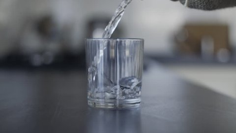 Hand Taking a Glass Man Drinking Cool Water. Not Completely Drunk Cup of Water Placed on the Kitchen Table. Bottle of Water Flows That Fills the Cup Hand is a Glass of Water and Takes It.