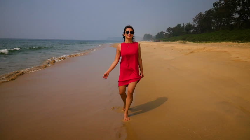 Beautiful woman in red dress walks at the sea side