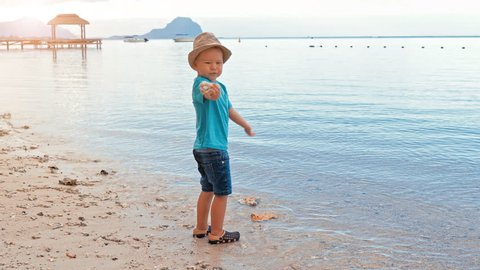 Cute boy throwing pebbles into the sea slow motion. Little boy plays on the beach, Le Morne Brabant UNESCO World Heritage Site in background, Mauritius