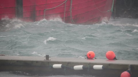 Rough weather gale force rain storm waves sea spray on docks and moored ship