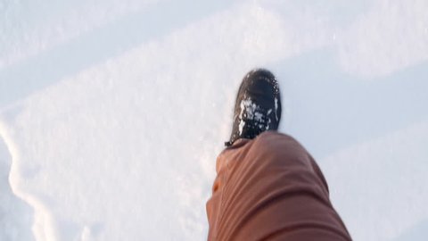 Looking down at men's feet walking through deep snow, in boots and jeans. slow motion