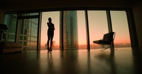 young woman businessman ceo talking on the phone, negotiating the panoramic windows in office skyscraper, sunset, dolly shot