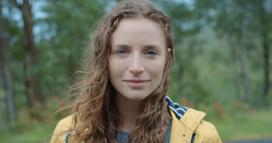 Close up portrait of Young Woman Smiling in nature with wet hair standing in rain Hiker Girl trekking cold stormy weather in Scotland Slow Motion