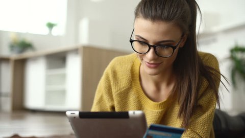 Young woman shopping online. Girl using digital tablet computer in home. Girl with tablet and bank card indoors. Easy pay using digital gadget.