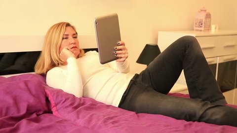 Attractive woman lying on a bed having a videochat with man on mobile digital tablet