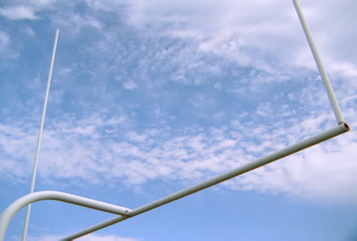 View of goalposts against sky with slow-motion football spiraling toward them and passing between uprights