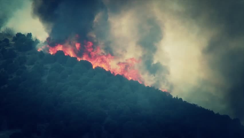 A raging wildfire burns across the mountain leaving a trail of smoke and ash.