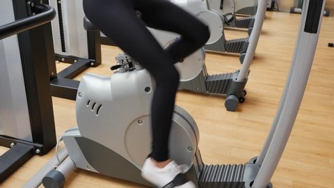 Tilt shot of a young brunette woman biking in the gym