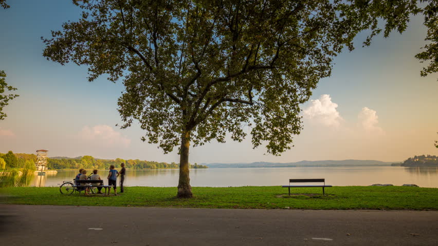 Time Lapse. lakeside sunset some people chat on a bench