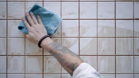 Tattooed male hand wipes out with blue micro fiber cloth dried and dirty tile adhesive from custom made kitchen table with white glance ceramic, top view
