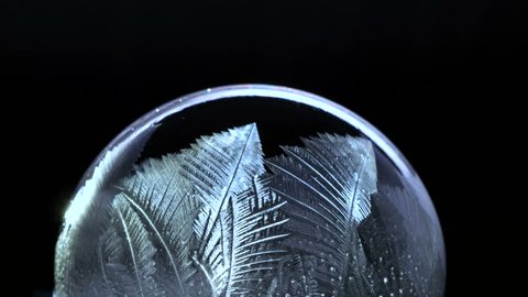 Winter Background. Frozen Soap Bubble with flying snowflakes inside. For Christmas and New Year Holidays exclusive backdrop. Ice patterns slowly grow on ball of soap against black copy space