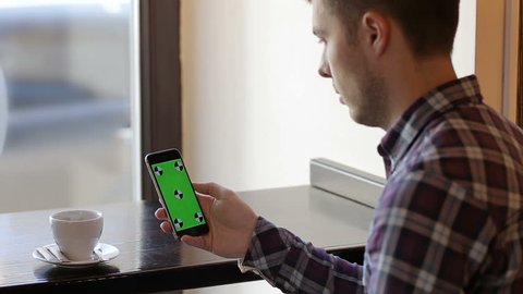 Man hold mobile cell phone with green touch screen in cafe