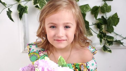 little blond girl in a green dress smelling a daisy flower in studio, slow motion