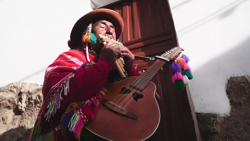 Native quechua man using a colorful handcrafted chullo and a highlander hat, singing with his guitar and quena on the alleys of Cusco Royalty-Free Stock Footage #24476030