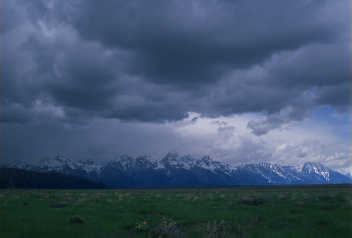 Time-lapse clouds flowing over prairie toward snow-capped mountains