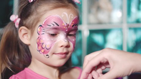 Painter hand draws face painting to little girl. Aqua makeup. Child with funny face painting. Medium close up.