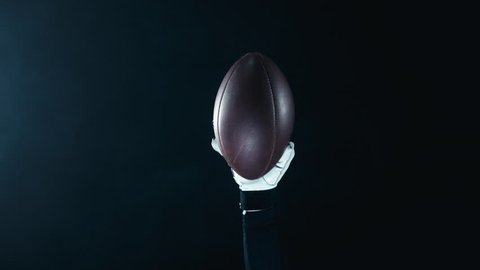 CU Caucasian male American football player rising a ball in his hand against black background Arkistovideo