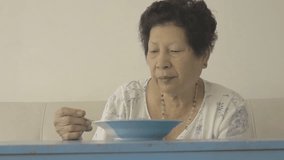 Asian senior woman eating food at home.  Senior sitting on sofa.