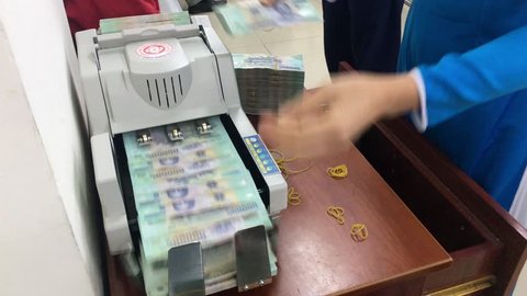 VUNG TAU, VIETNAM - FEBRUARY 20, 2017: A woman puts dongs (Vietnamese national currency) in a counting machine and stacks them in packs at a Vietcombank branch.