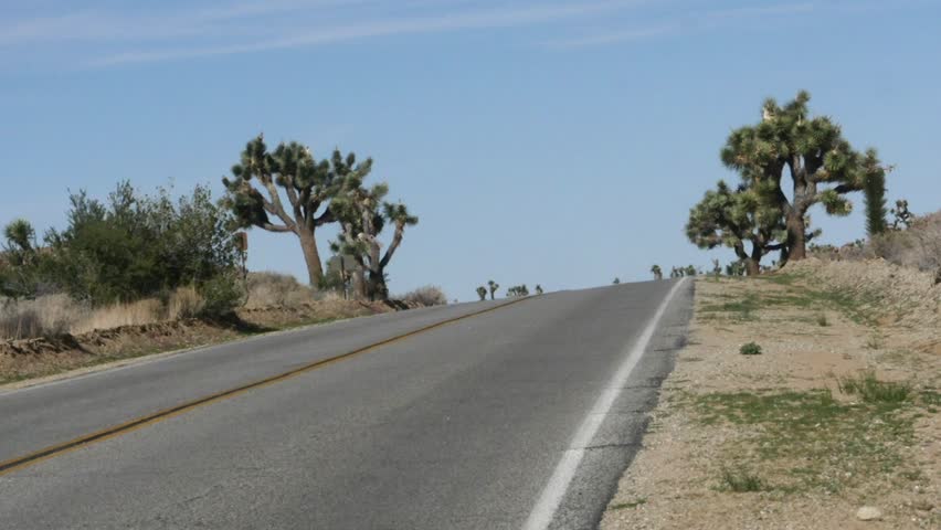 Zoom out time lapse of cars driving on a asphalt road in Joshua tree national park, in California, United states of america.