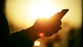 Silhouette of unrecognizable woman using a smart phone with beautiful sunset light in the background